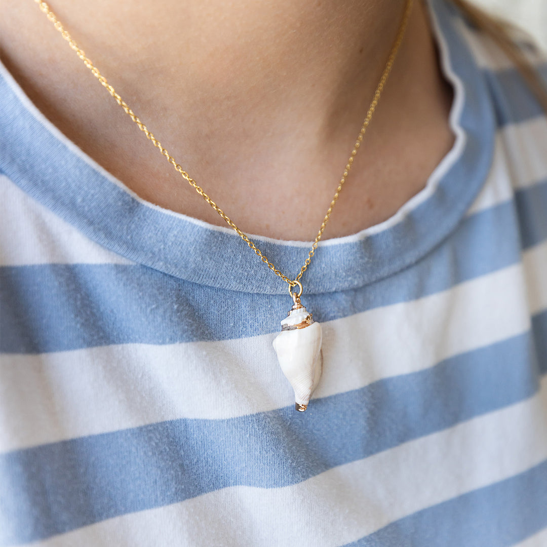 A person wearing a light blue and white striped shirt wears a seashell necklace with a gold chain.