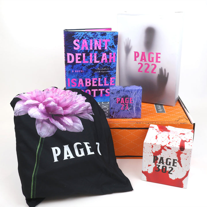 A hardcover edition of Saint Delilah stands on an orange OUABC Halloween box next to two themed wrapped gifts labeled with page numbers. In front of the box are two more wrapped gifts labeled with page numbers.