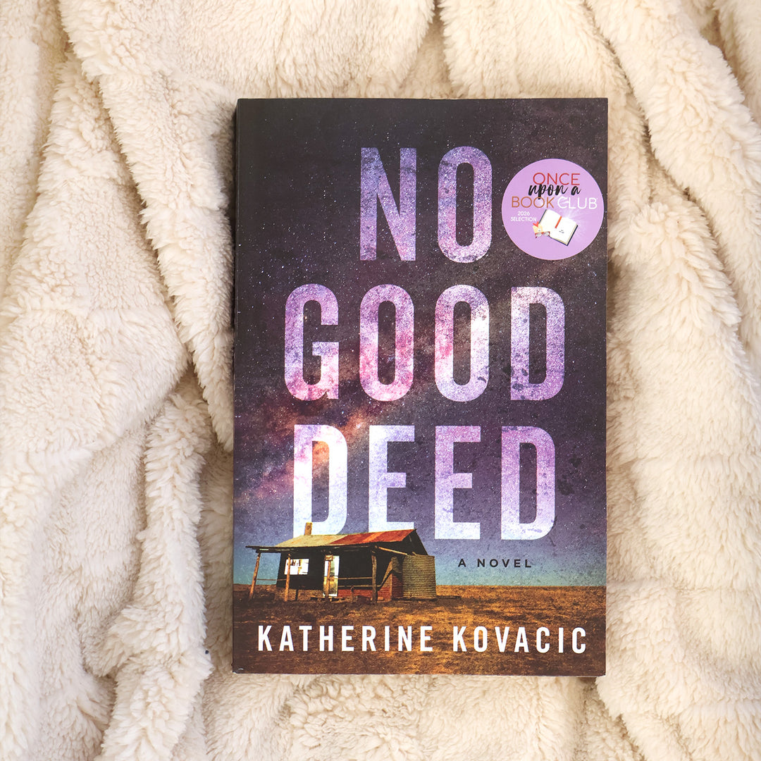 The book cover of 'No Good Deed' by Katherine Kovacic, displayed flat on a soft, cream-colored fleece blanket. The cover features a dark purple and black starry sky with a small cabin at the bottom and a purple 'Once Upon a Book Club' badge in the top right corner.