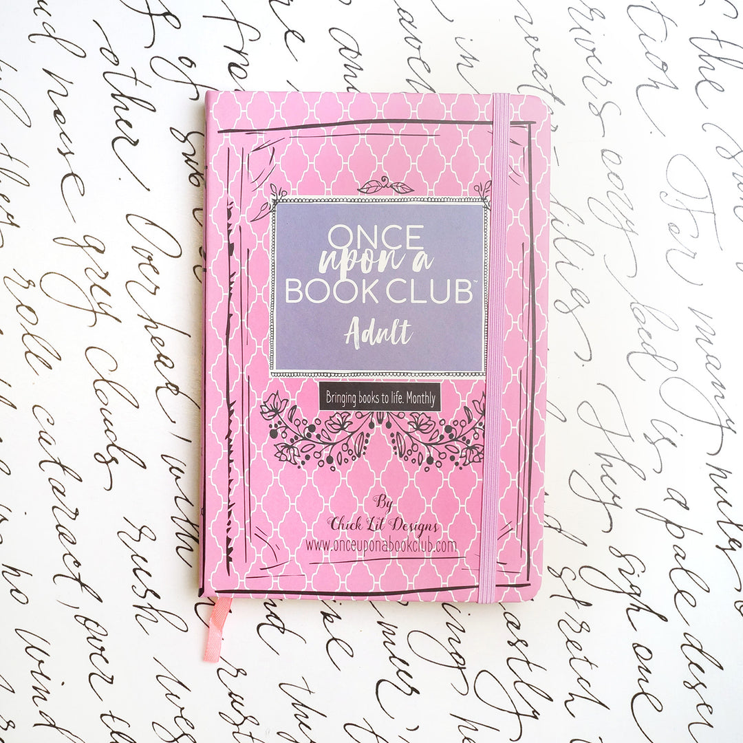 A pink Once Upon a Book Club notebook sits on a white background decorated with script.