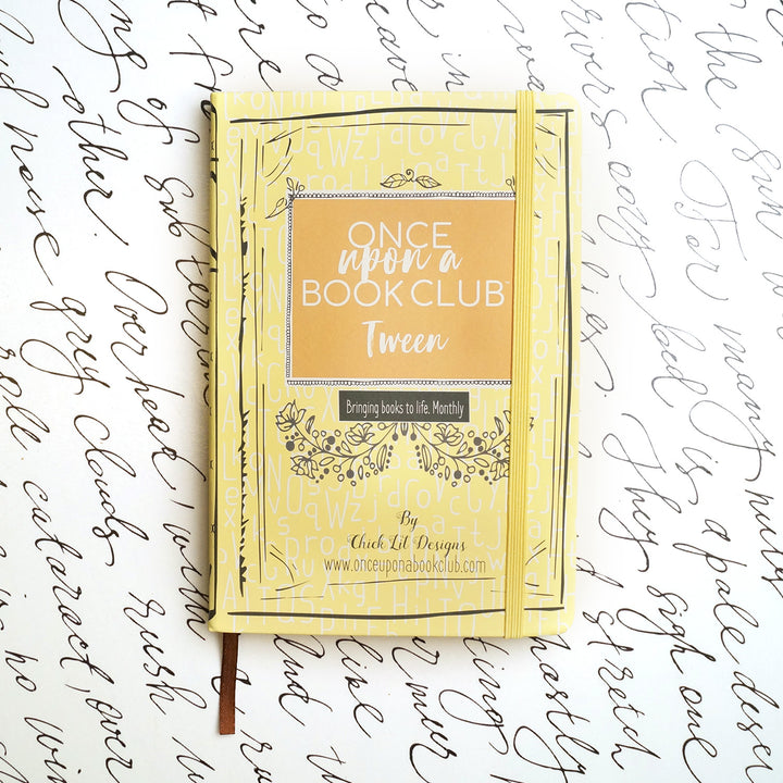 A yellow Once Upon a Book Club notebook sits on a white background decorated with script.