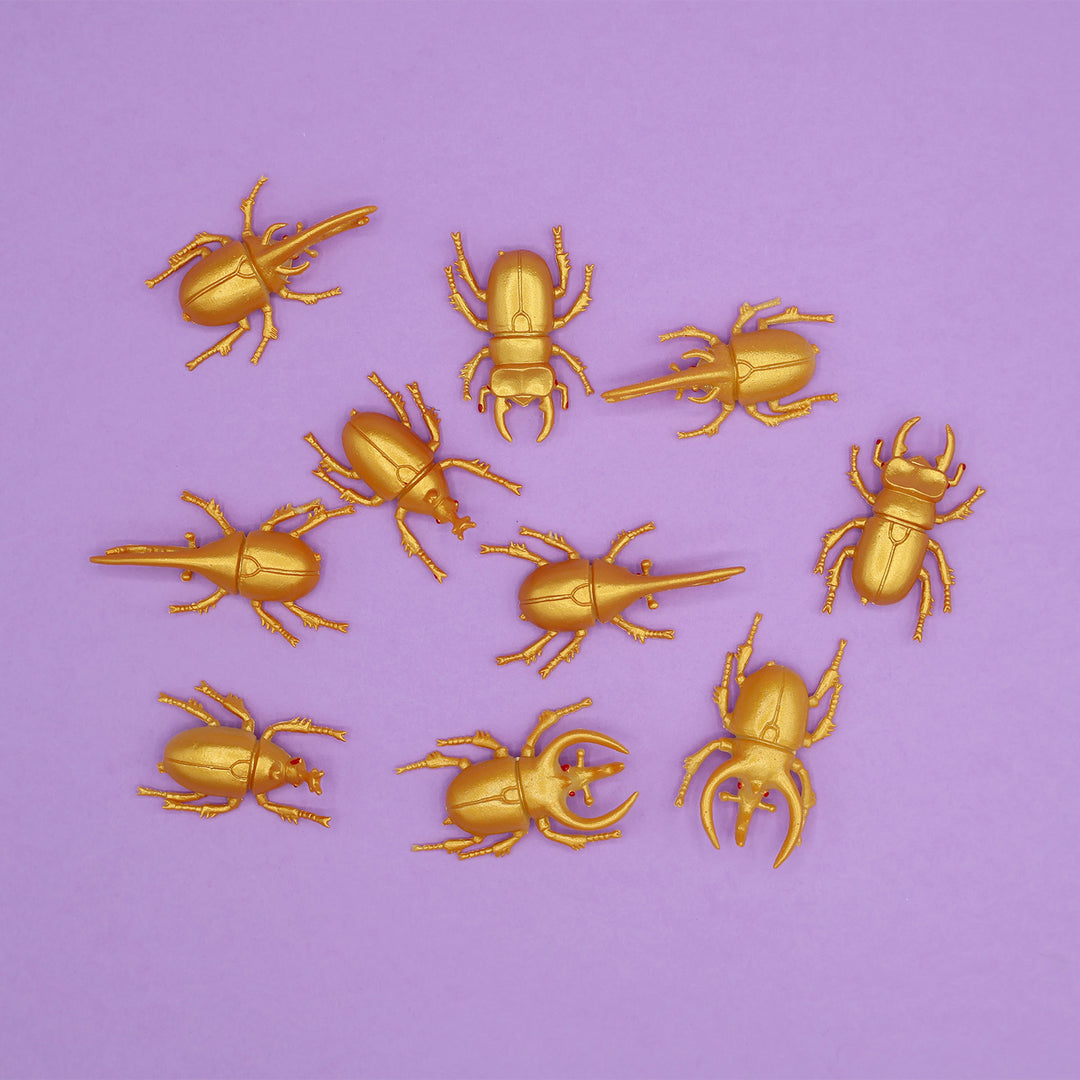 Ten fake golden beetles across a light purple background
