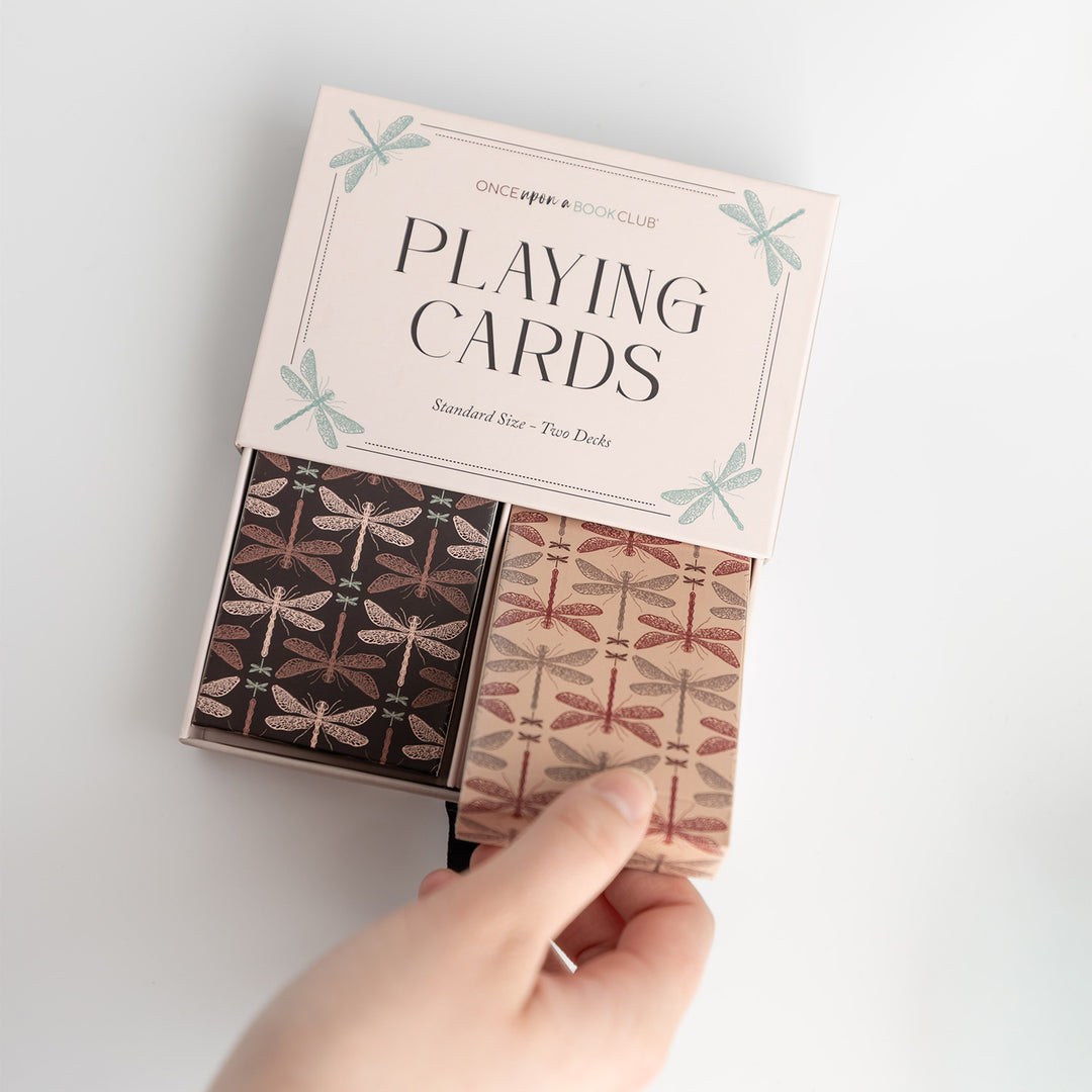 An open box showing two sets of standard size playing cards. The cards have a black and brown dragonfly pattern on their backs.