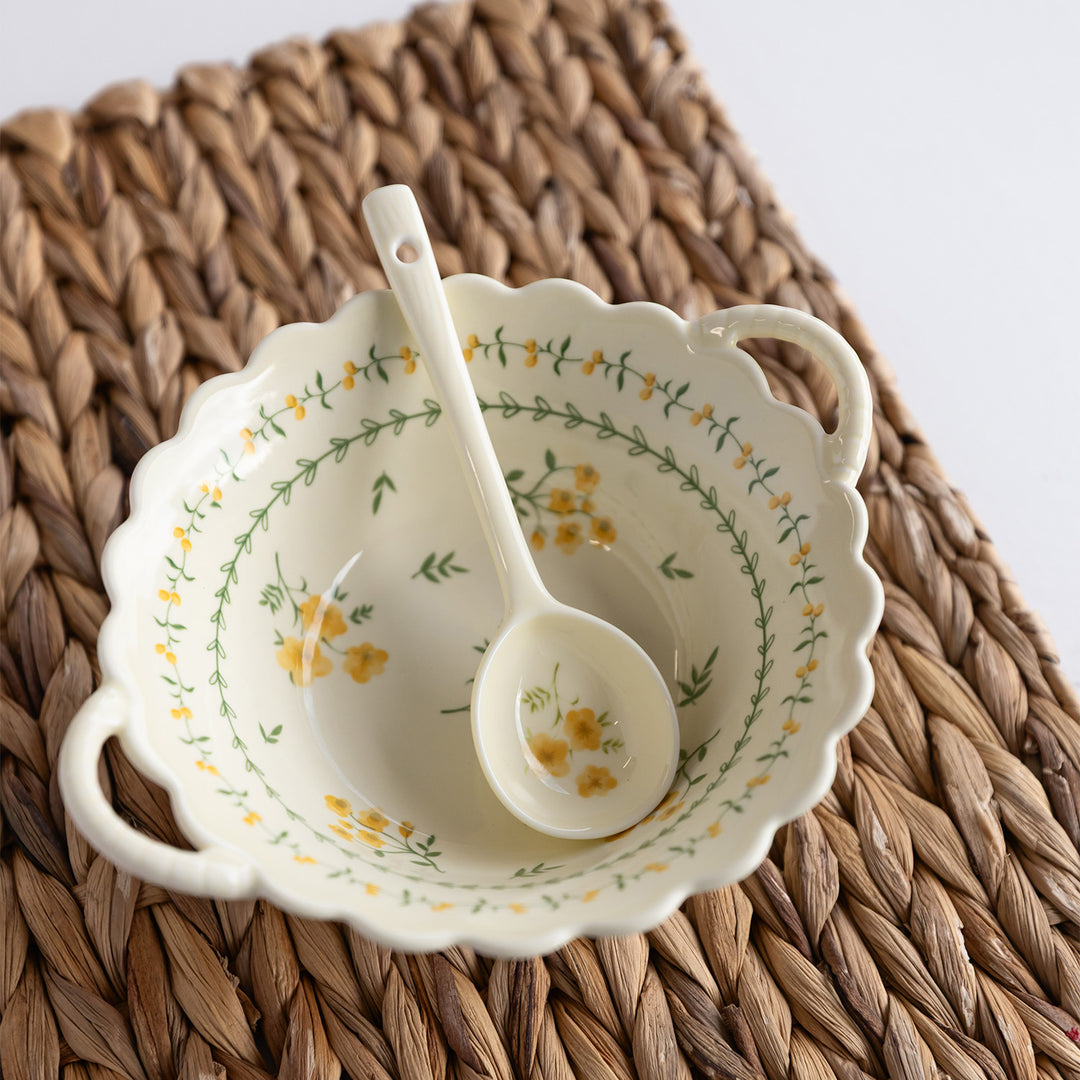 A white ceramic soup bowl with yellow and green floral pattern and a matching spoon.