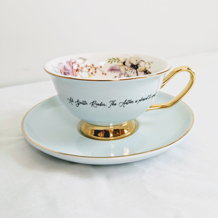 a light blue teacup with gold detail and a quote printed on the outside of it with floral details printed on the inside.