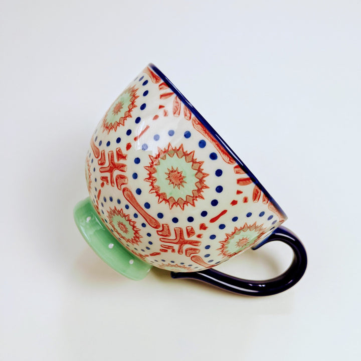 An oversized mug painted with a dark blue, red, and light blue pattern sits on a white background.