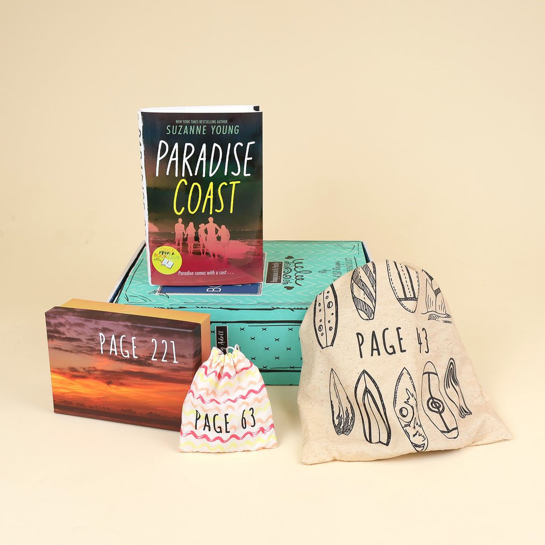A hardcover copy of Paradise Coast by Suzanne Young lays on a green OUABC box and is surrounded by three wrapped gifts labeled with page numbers.