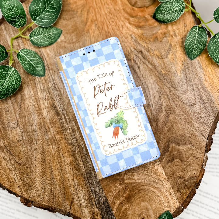 Phone case with 'The Tale of Peter Rabbit' design on a wooden surface with leaves.