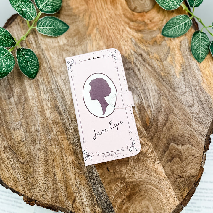 The front cover of a phone case inspired by Jane Eyre by Charlotte Bronte. The phone case sits on a wood slice surrounded by greenery.