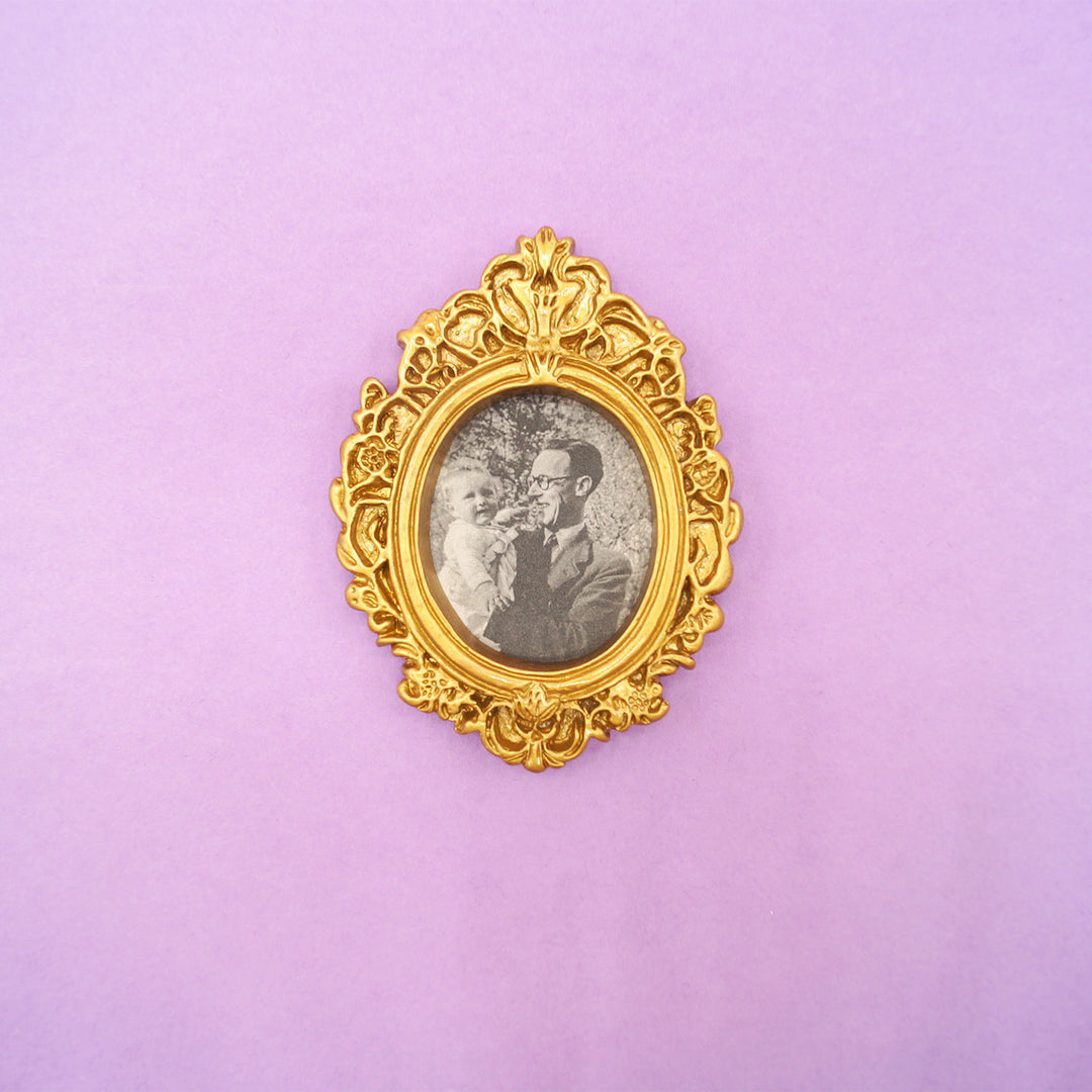 a small gold ornate picture frame with magnet on the back. sits on a purple background.