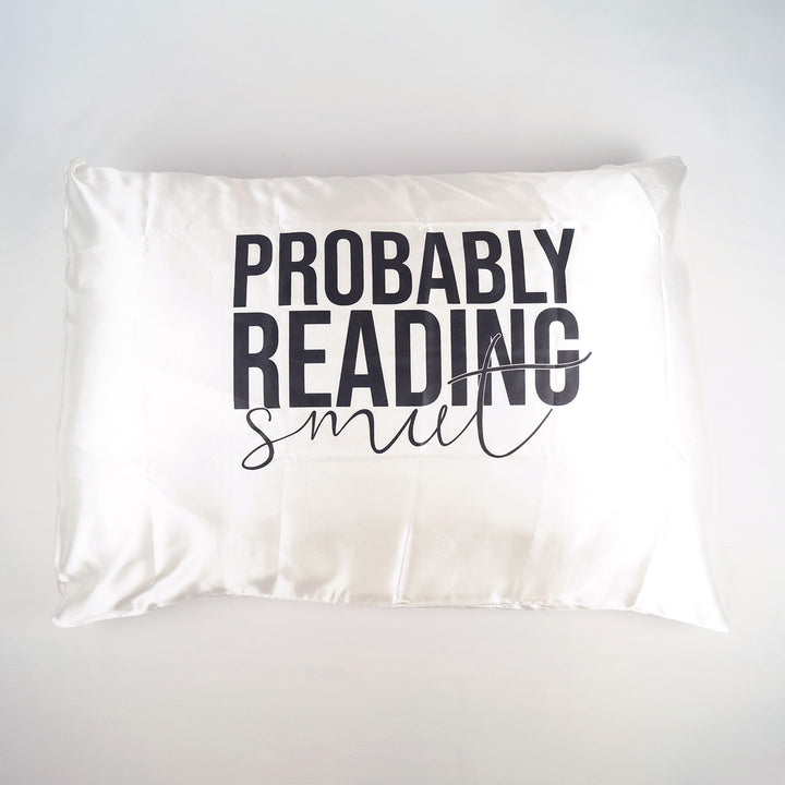 a white satin standard size pillow case with black lettering that says "Probably Reading Smut"