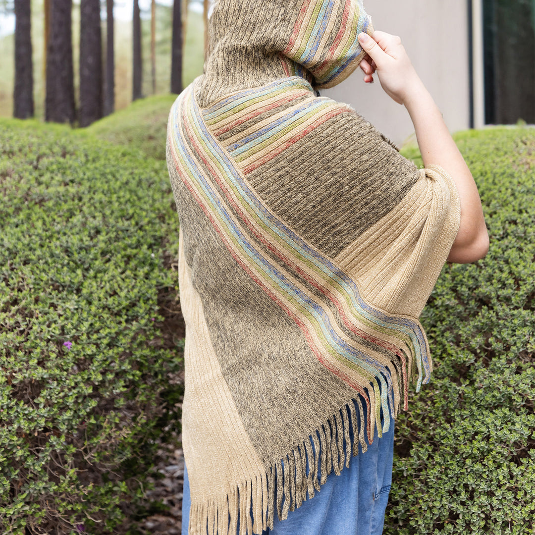 A woman wears a tan hooded poncho with a line of rainbow colors across one side.
