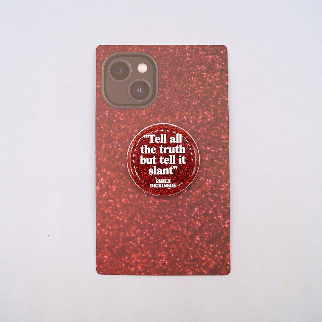 A red glittery phone grip with an Emily Dickinson quote "Tell all the truth but tell it slant" on a red glittery phone background to show what it will look like when attached to your phone.