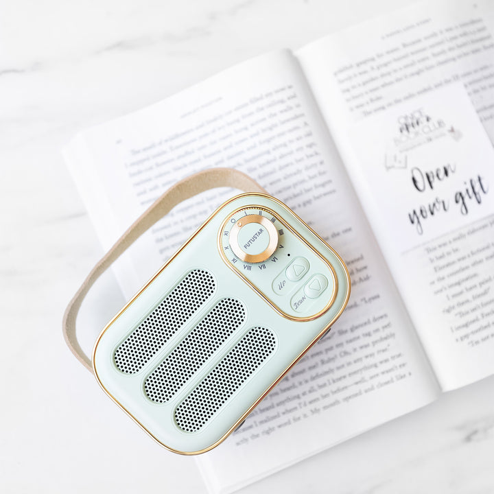 a miniature mint green bluetooth radio lays on an open book with an Open Your Gift sticky note.