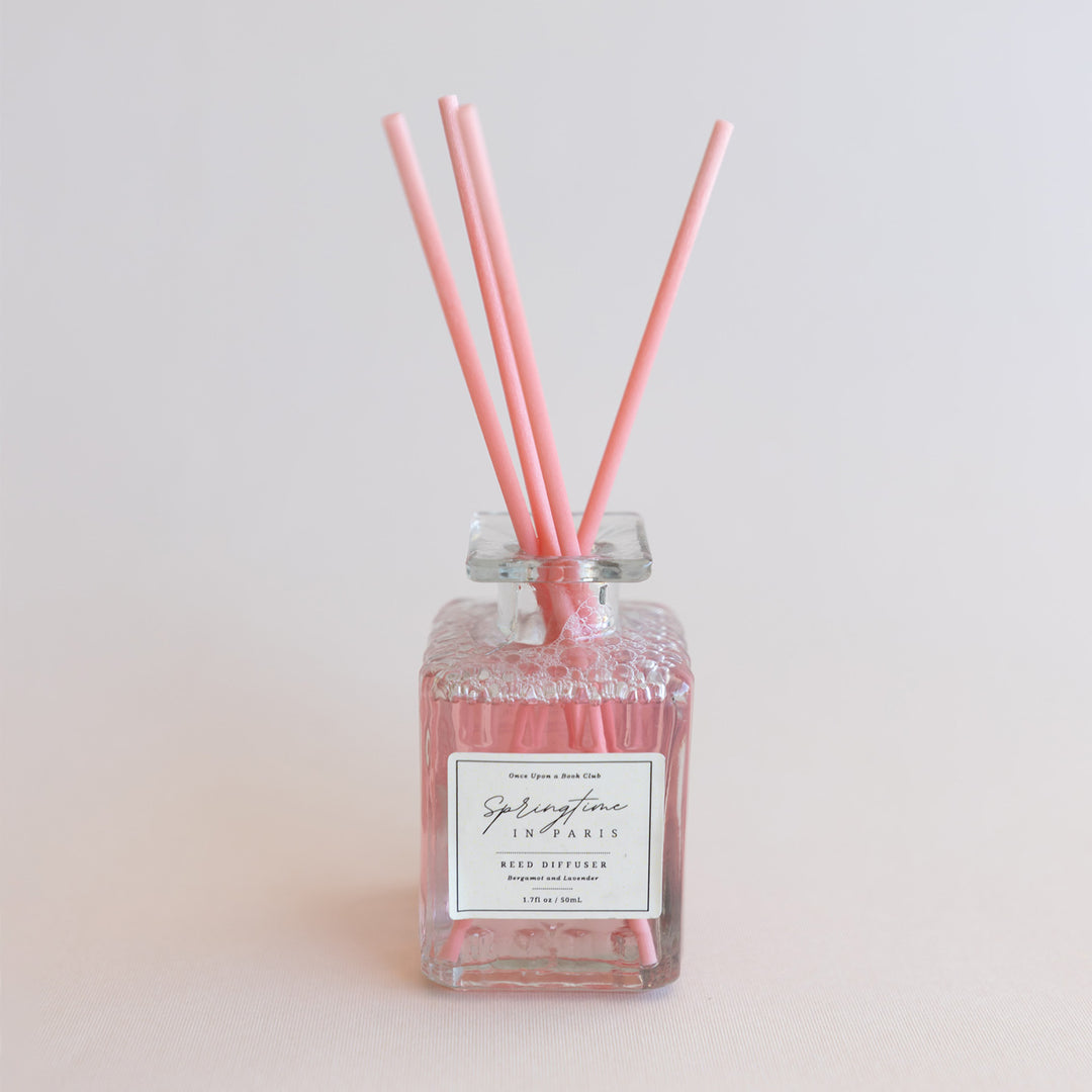 A pink reed diffuser with four pink reeds sticking out the top. The label on the clear bottle says Springtime in Paris Reed Diffuser.