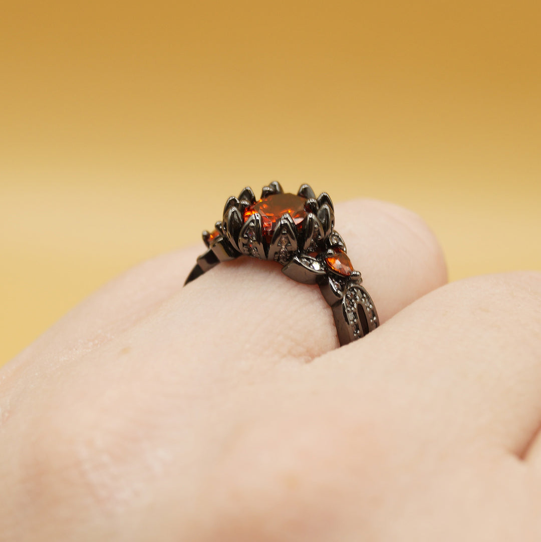 a white hand wears a black ring with a red gemstone in the center 