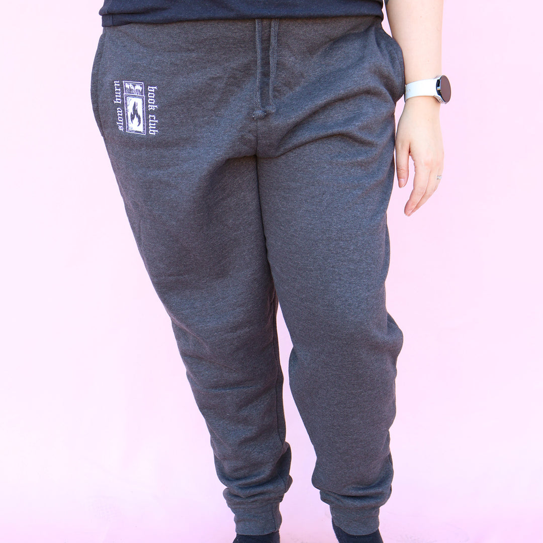 Gray sweatpants with embroidered 'Slow Burn Book Club' and matchbook design on a pink background