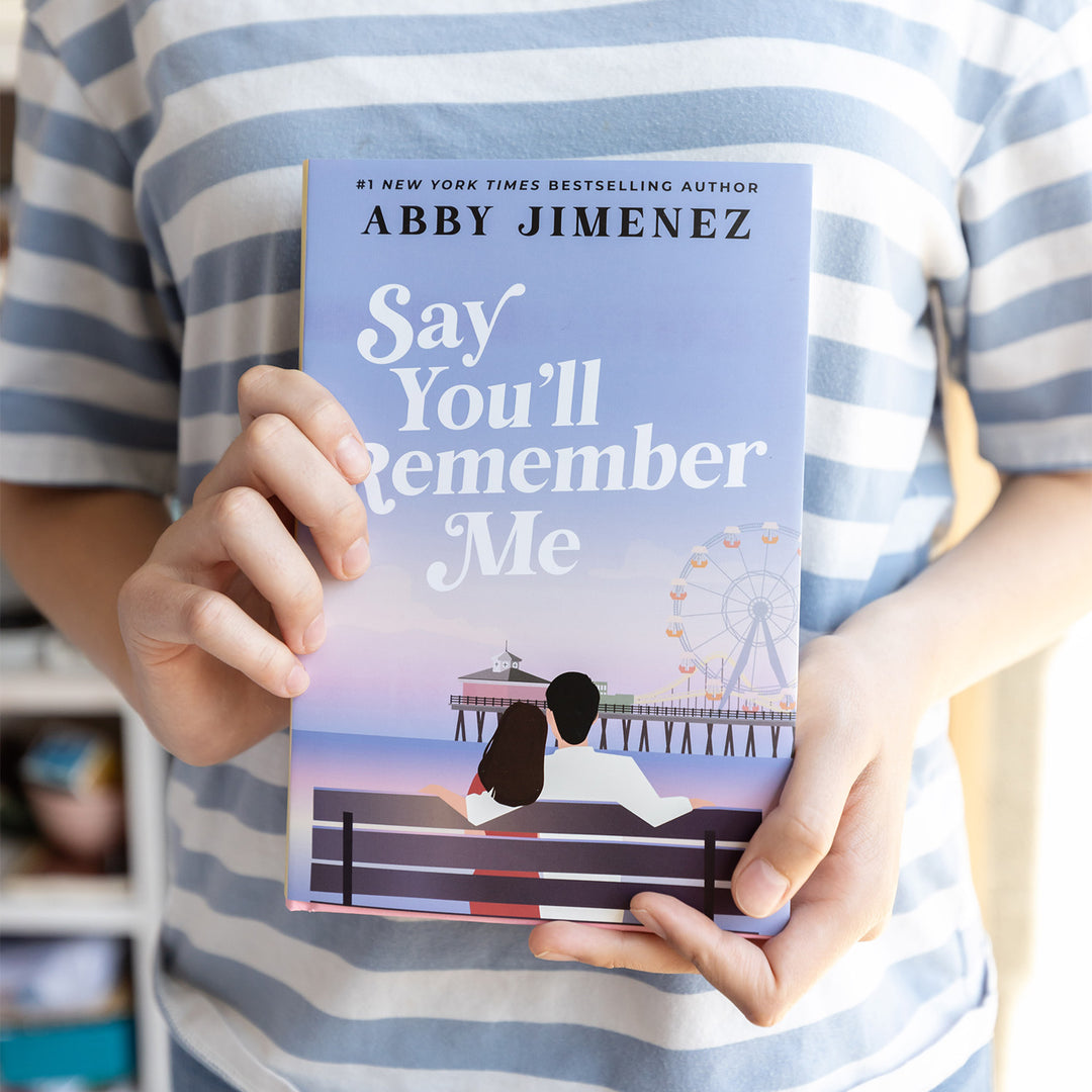 'Say You'll Remember Me' by Abby Jimenez held by a person showing side 2 of the dust jacket featuring the exclusive artwork.