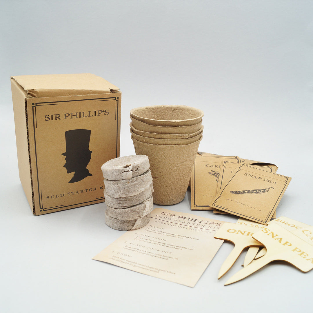 A brown box sits next to four soil starter pods, compostable pots, seed packets, four small wooden signs, and instructions to grow your garden