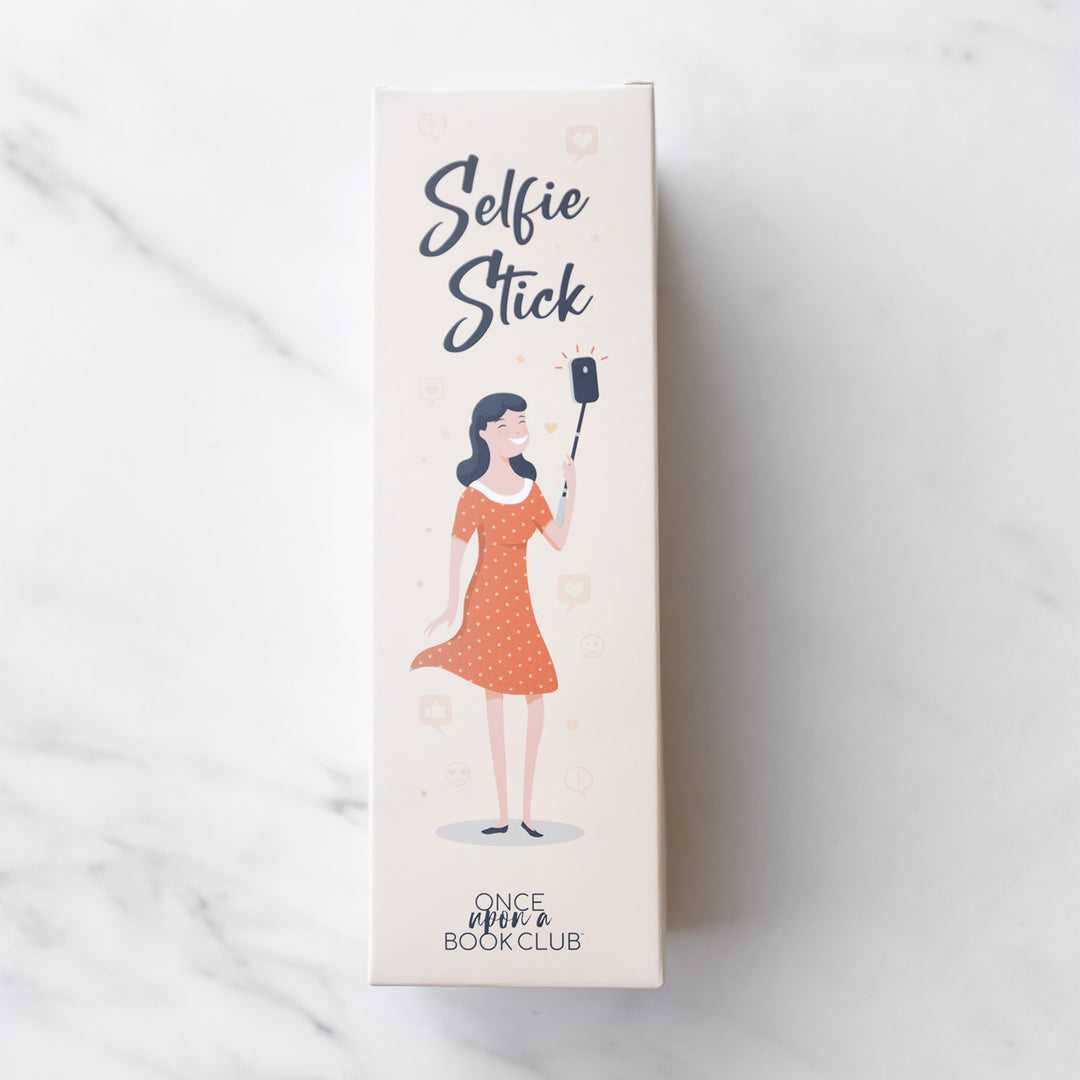 A beige box labeled Selfie Stick with a drawing of a woman in an orange dress using a selfie stick.