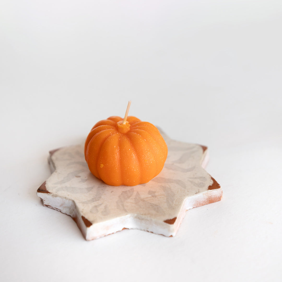 A pumpkin-shaped orange candle sits on a piece of star-shaped pottery.