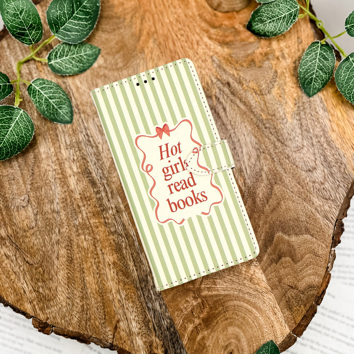 Notebook with 'Hot girl read books' text on a wooden surface with green leaves.