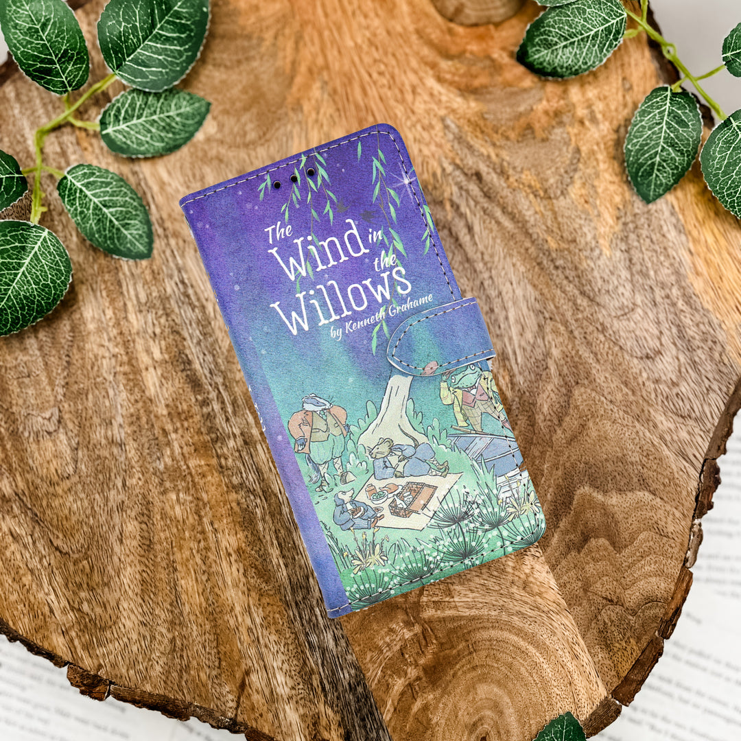 Phone case with 'The Wind in the Willows' design on a wooden surface with leaves.