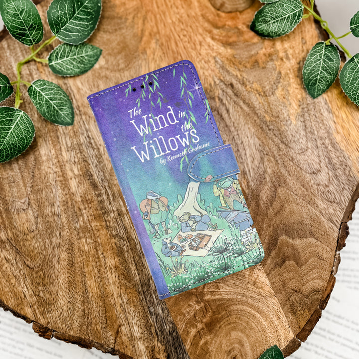 Phone case with 'The Wind in the Willows' design on a wooden surface with leaves.