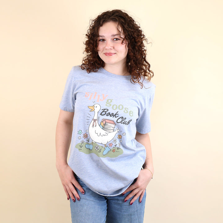 A woman wearing a light blue t-shirt with a Silly Goose Book Club graphic and text on a beige background