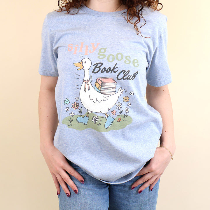 A woman wearing a light blue t-shirt with a Silly Goose Book Club graphic and text on a beige background