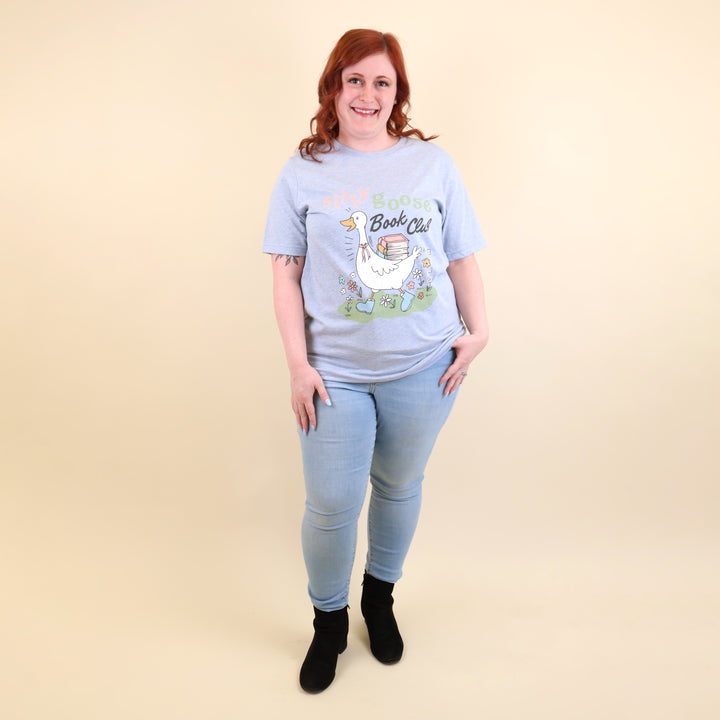 A woman wearing a light blue t-shirt with a Silly Goose Book Club graphic and text on a beige background