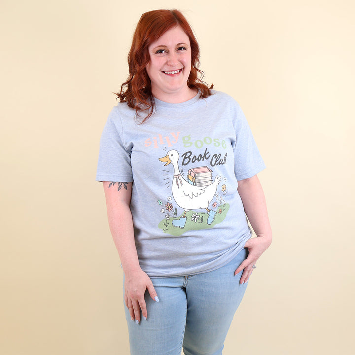 A woman wearing a light blue t-shirt with a Silly Goose Book Club graphic and text on a beige background