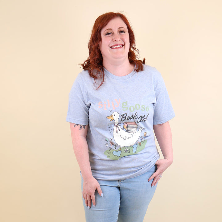 A woman wearing a light blue t-shirt with a Silly Goose Book Club graphic and text on a beige background