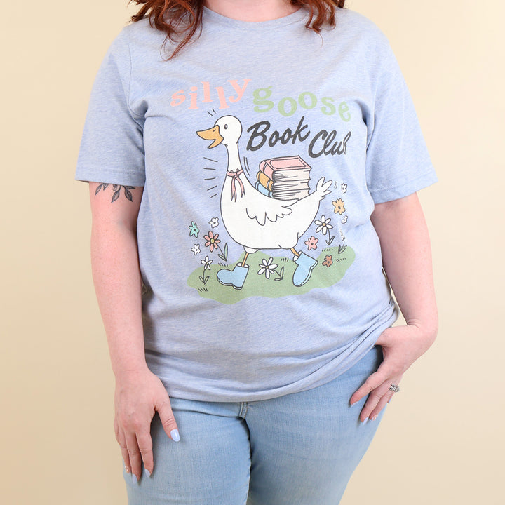 A woman wearing a light blue t-shirt with a Silly Goose Book Club graphic and text on a beige background