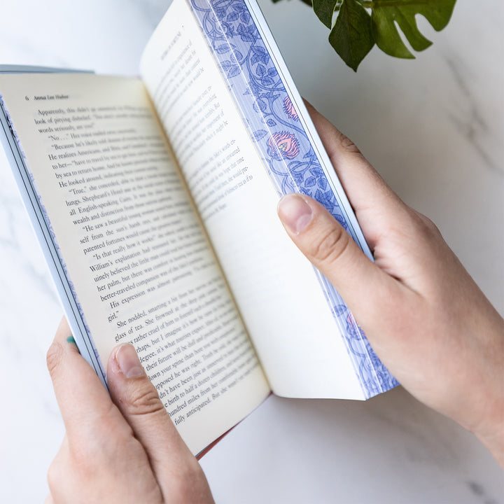 An exclusively designed hardcover copy of Sisters of Fortune by Anne Lee Huber as designed by the Once Upon a Book Club team. The sprayed edges are purple with pink and yellow details in a design by William Morris.