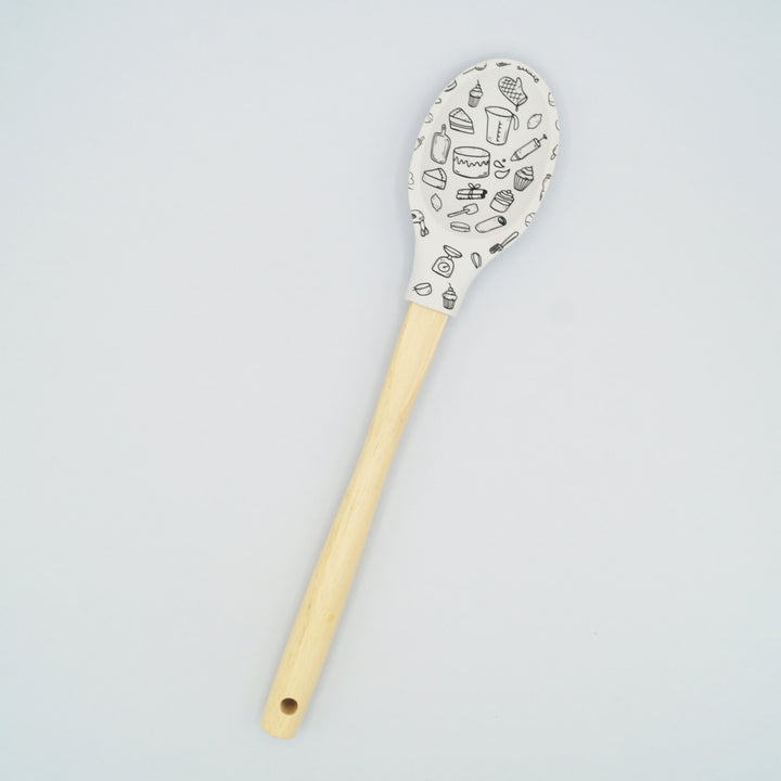 A white silicone cooking spoon with a wooden handle. There is a pattern of kitchen appliances of the silicone part.