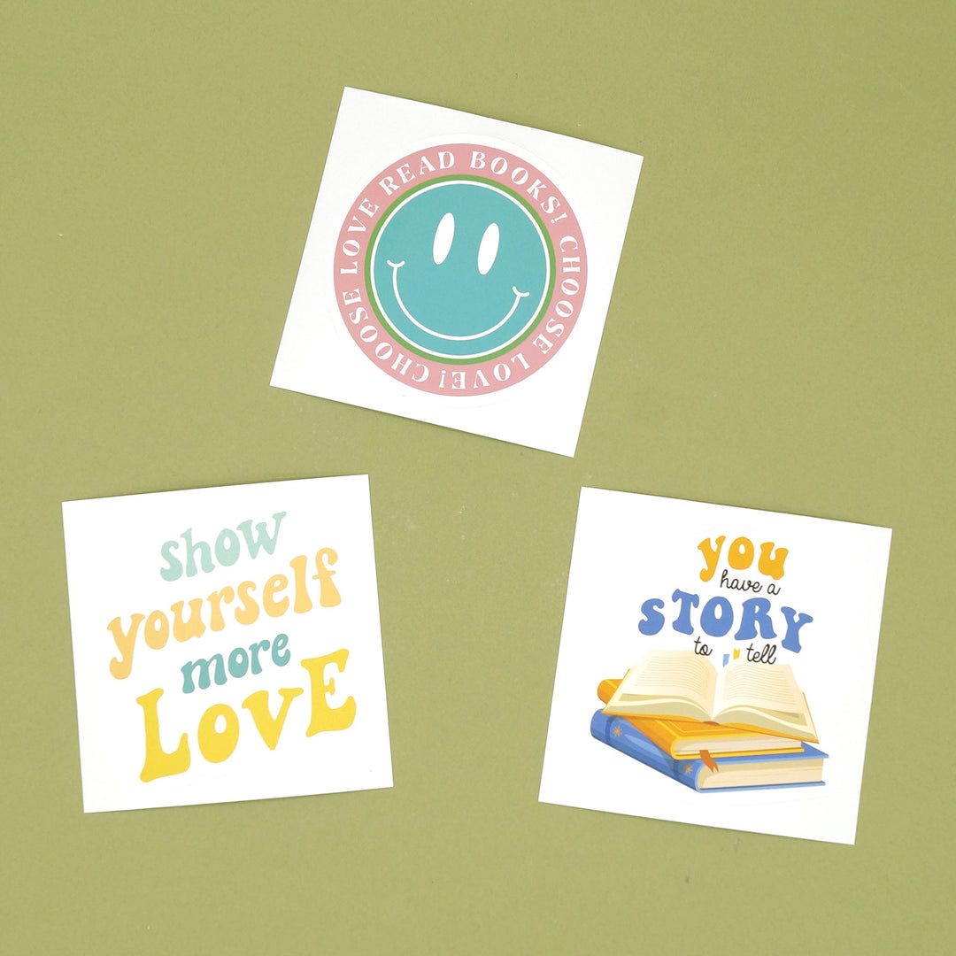 A set of three vinyl stickers on a green background. One is a smiley face with the words Choose Love! Read Books! One is a quote sticker with the words Show Yourself More Love and one is a stack of books with the words You Have a Story to Tell above them.