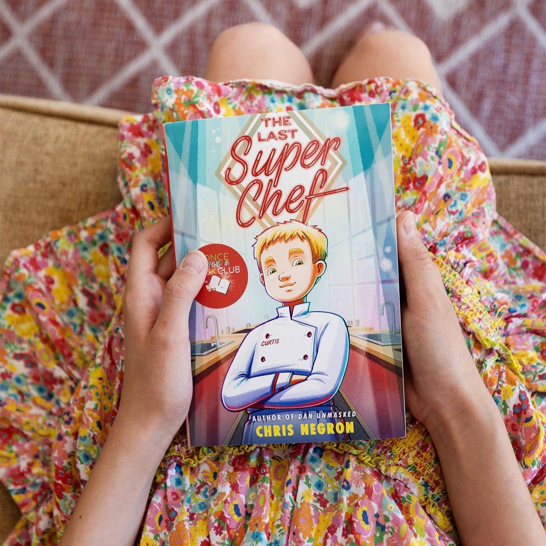 Person holding a book titled 'The Last Super Chef' by Chris Negron on a colorful fabric background.