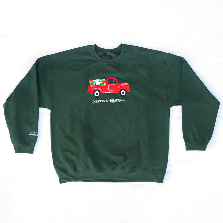 A forest green embroidered sweatshirt with a red pickup truck filled with books. Under the truck are the embroidered words "Season's Readings". On the right sleeve is a little white embroidered open book.