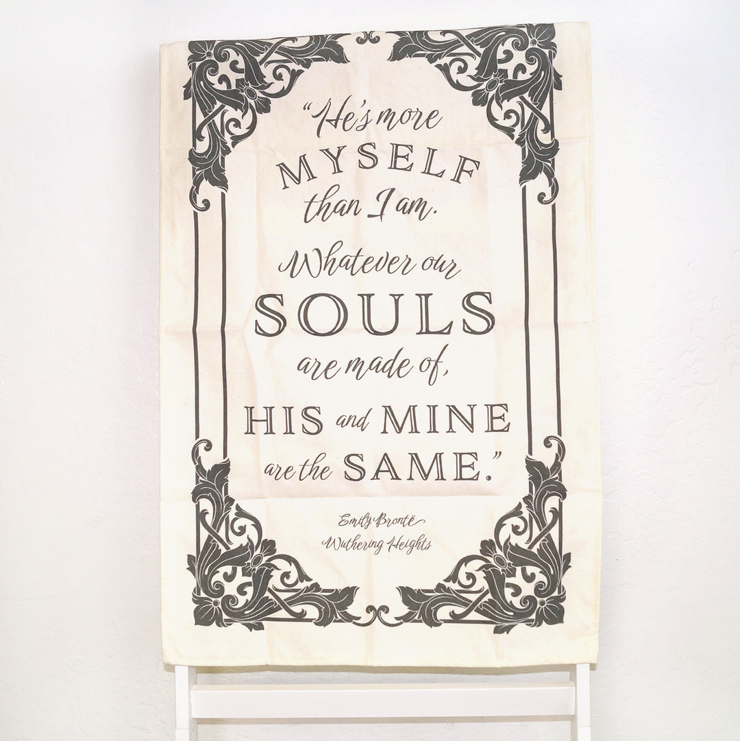 A white tea towel with the quote He's more myself than I am. Whatever our souls are made of, his and mine are the same. Emily Bronte Wuthering Heights. The words are in black script font within a framed design