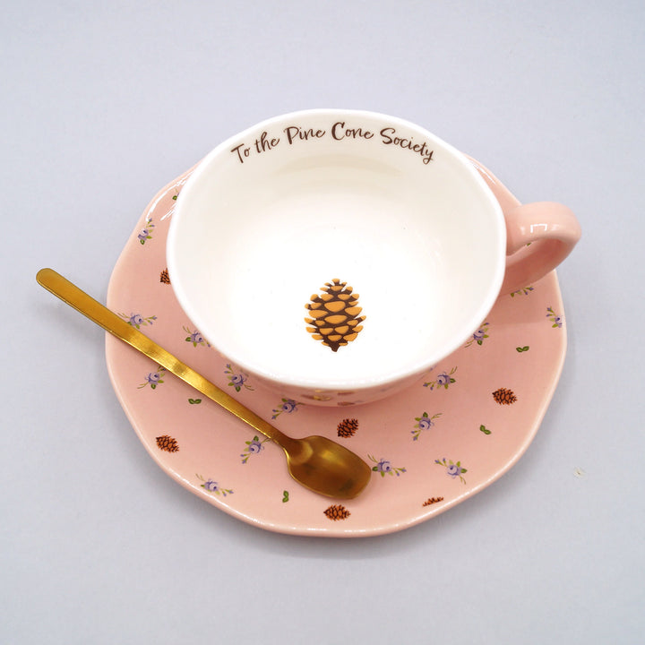 A pink floral and pine cone detailed teacup, saucer, and gold teaspoon