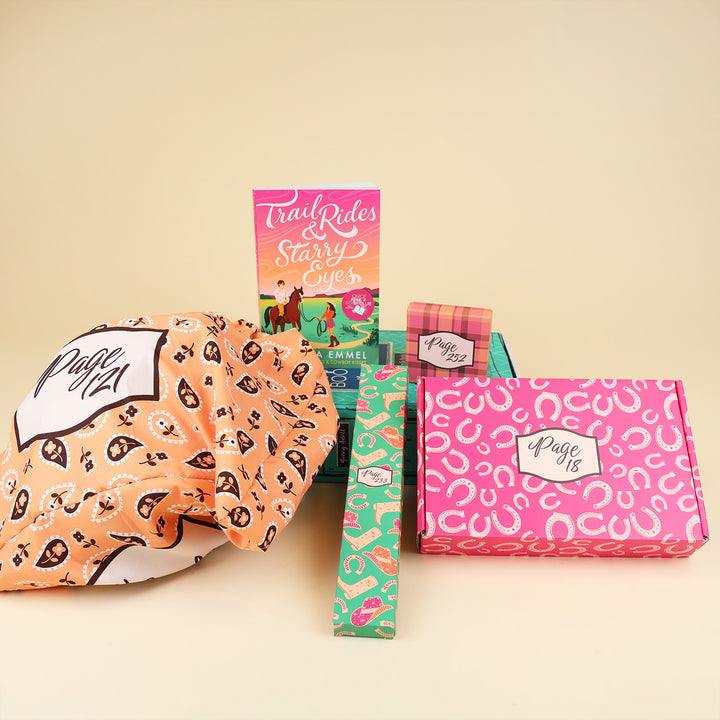 A paperback edition of Trail Rides and Starry Eyes stands on a green OUABC box next to a small box labeled with a page number. In front of the OUABC box are three wrapped gifts labeled with page numbers.