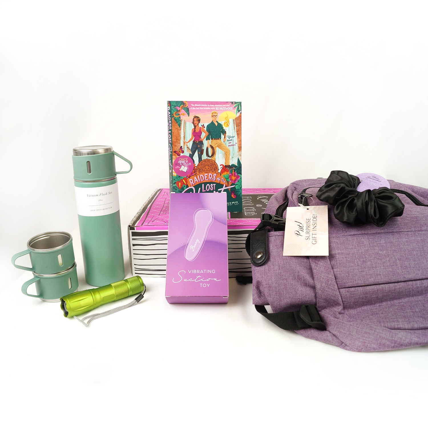 A paperback edition of Raiders of the Lost Heart is on a pink Once Upon a Book Club box. In front of the box are a mint green vacuum flask set, green flashlight, pink box labeled Vibrating Suction Toy, and purple backpack. On top of the backpack is a black scrunchie.