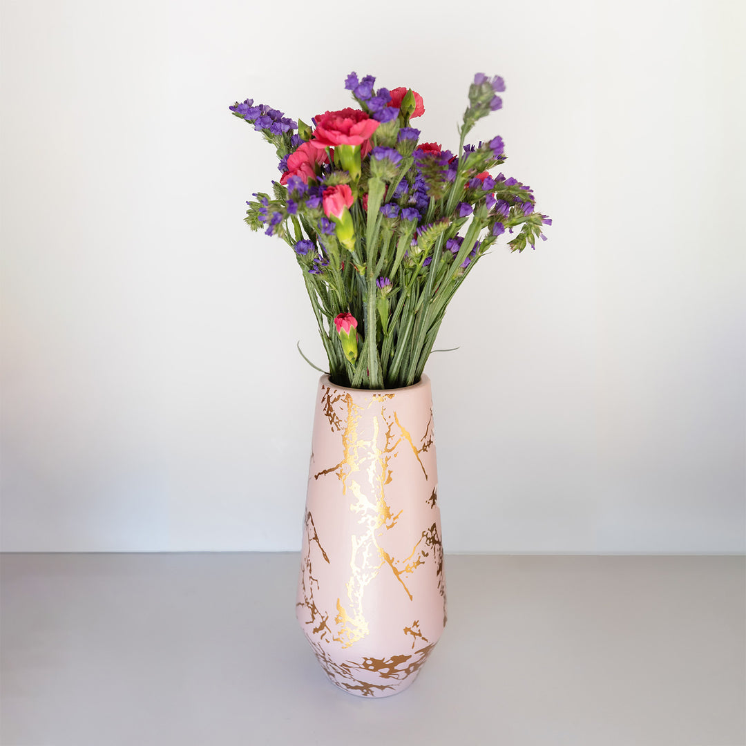 A light pink vase with gold foil marbled design, holding a bouquet of pink and purple flowers.