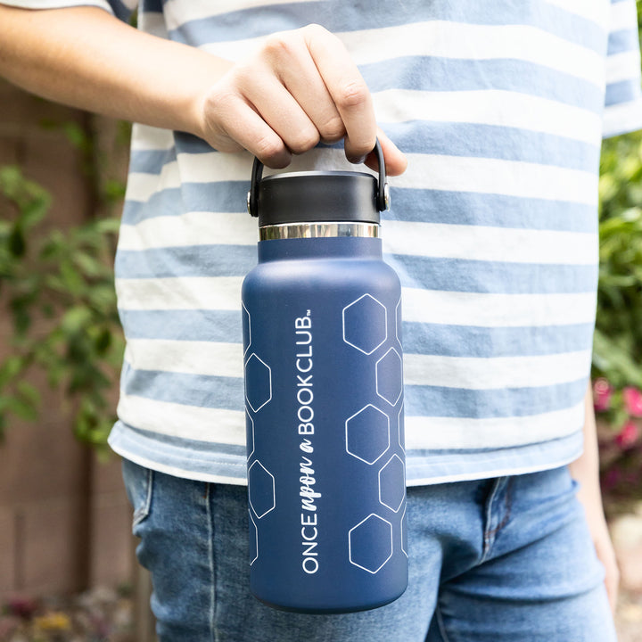 A white hand holds a dark blue water bottle by the black rubber handle. The white writing is visible in the shot.