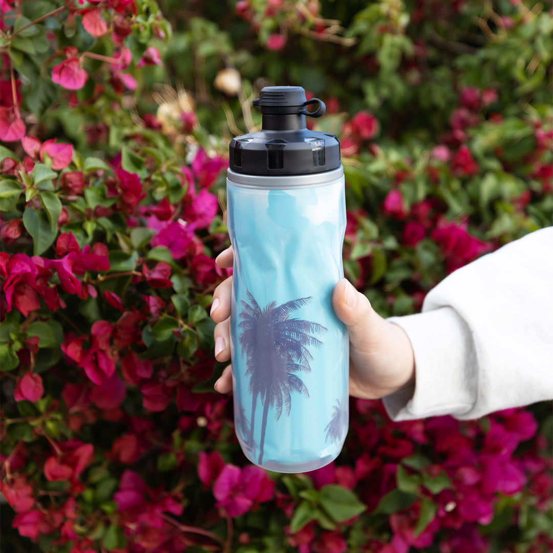 Hand holding a water bottle with blue palm tree design against a floral background