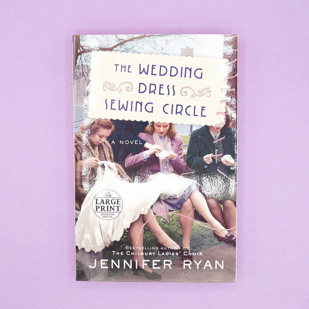 A paperback, large print edition of The Wedding Dress Sewing Circle by Jennifer Ryan sits on a purple background.