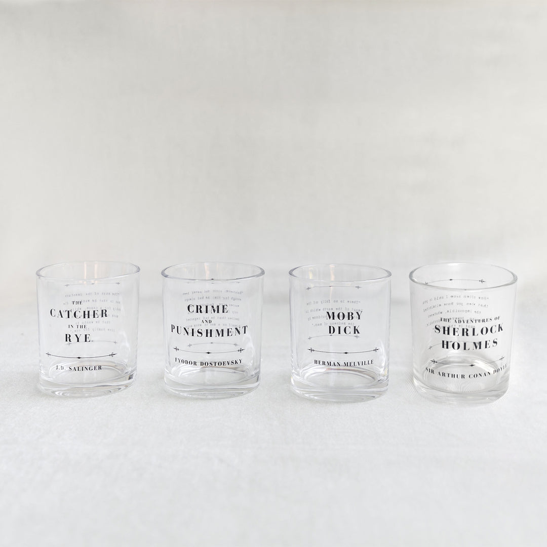 A set of whiskey glasses inspired by classic book titles. The four titles in order from left to right are The Catcher in the Rye by J.D. Salinger, Crime and Punishment by Fyodor Dostoevsky, Moby Dick by Herman Melville, and The Adventures of Sherlock Holmes by Sir Arthur Conan Doyle.