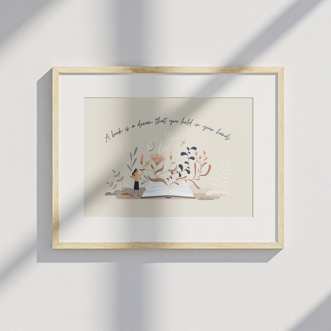 A matted wooden frame hangs on a white wall and displays the "Books are Dreams" art print. A shadow from a window is visible over the art print.