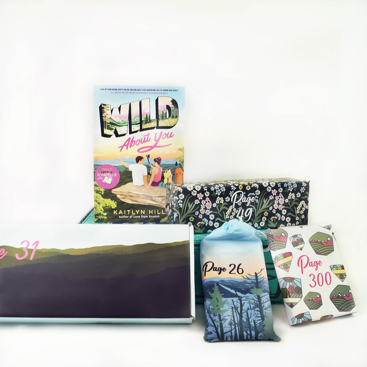 A paperback copy of Wild About You by Kaitlyn Hill sits on a green Once Upon a Book Club young adult box. This box is surrounded by wrapped gifts labeled with page numbers.